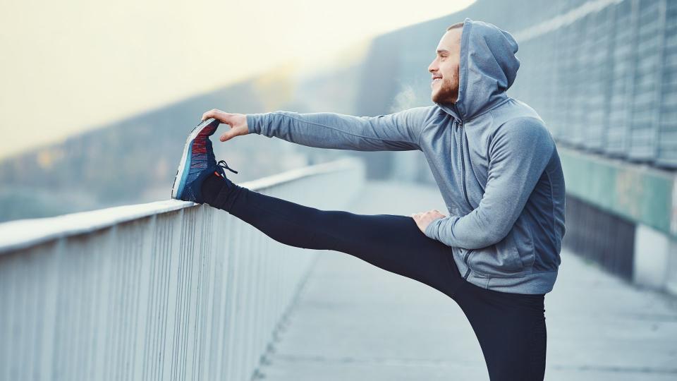 Male runner doing stretching exercise, preparing for morning workout in the park