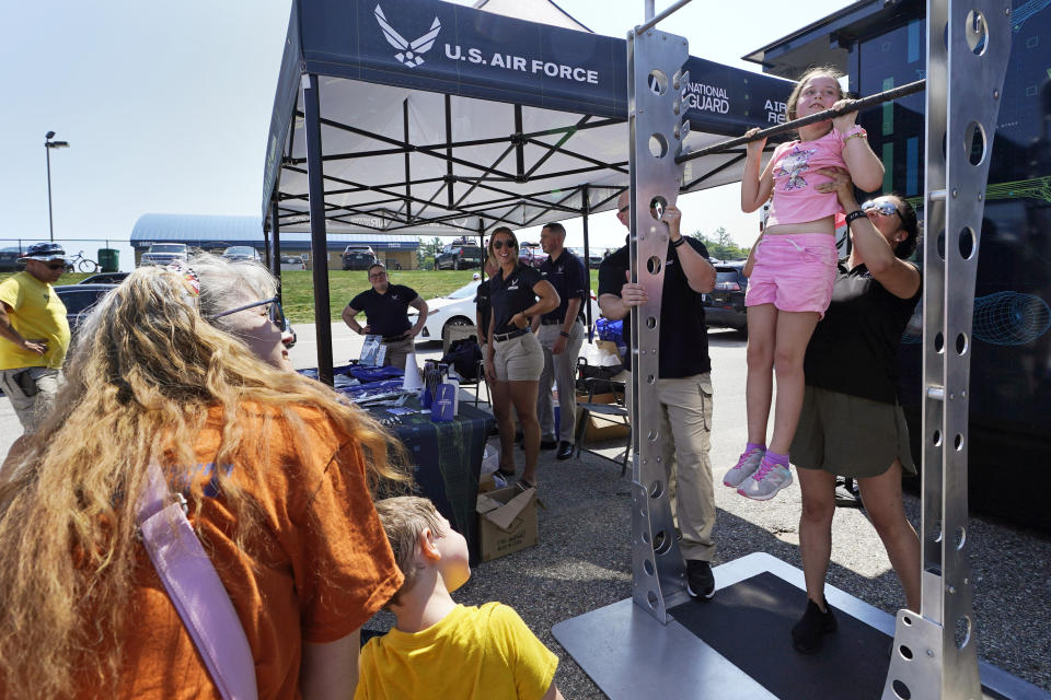 Aubrey White, 10, is helped while hanging on a chin-up bar while stopping at the U.S. Air Force recruiting tent prior to a NASCAR race at the New Hampshire Motor Speedway, Sunday, July 17, 2022, in Loudon, N.H. These are tough times for military recruiters. All services are having problems finding young people who want to join and can meet the physical, mental and moral requirements. Recruiters are offering bigger bonuses and other incentives to those who sign up. And they are seizing on the boost that Hollywood may offer – such as the buzz over Top Gun. (AP Photo/Charles Krupa)