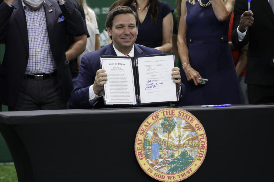 FILE - Florida Gov. Ron DeSantis holds up a just signed bill which would allow college athletes in the state to earn money from endorsement deals, at the University of Miami in Coral Gables, Fla., in this Friday, June 12, 2020, file photo. The NCAA Board of Directors is expected to greenlight one of the biggest changes in the history of college athletics when it clears the way for athletes to start earning money based on their fame and celebrity without fear of endangering their eligibility or putting their school in jeopardy of violating amateurism rules that have stood for decades.(AP Photo/Lynne Sladky, File)