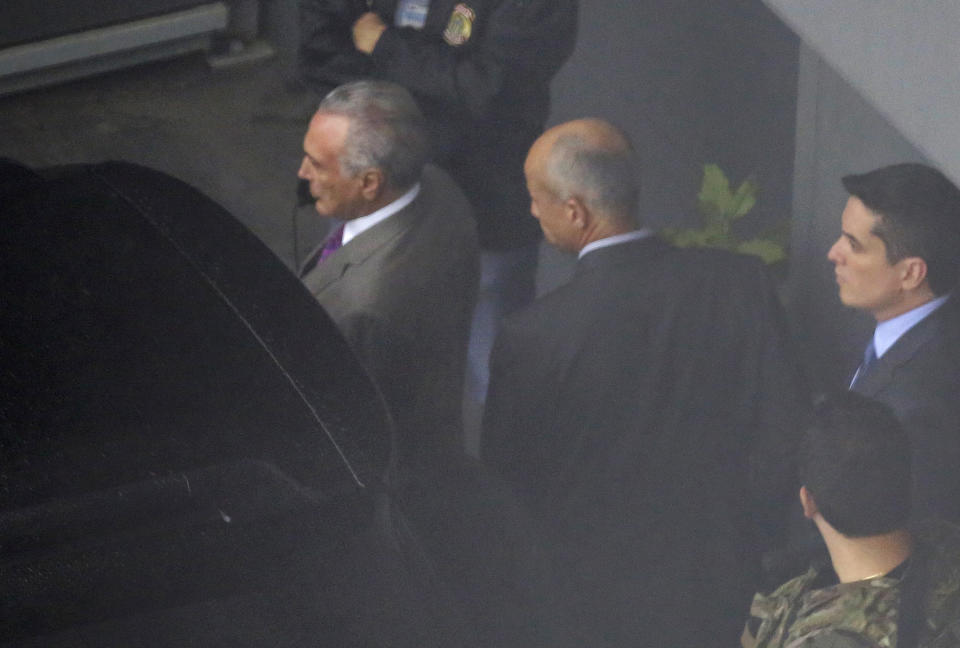 Fotografía tomada a través de una valla en la que se aprecia al expresidente brasileño Michel Temer, a la izquierda, en el aeropuerto internacional de Sao Paulo, Brasil, la noche del jueves 21 de marzo de 2019. (AP Foto/Nelson Antoine)