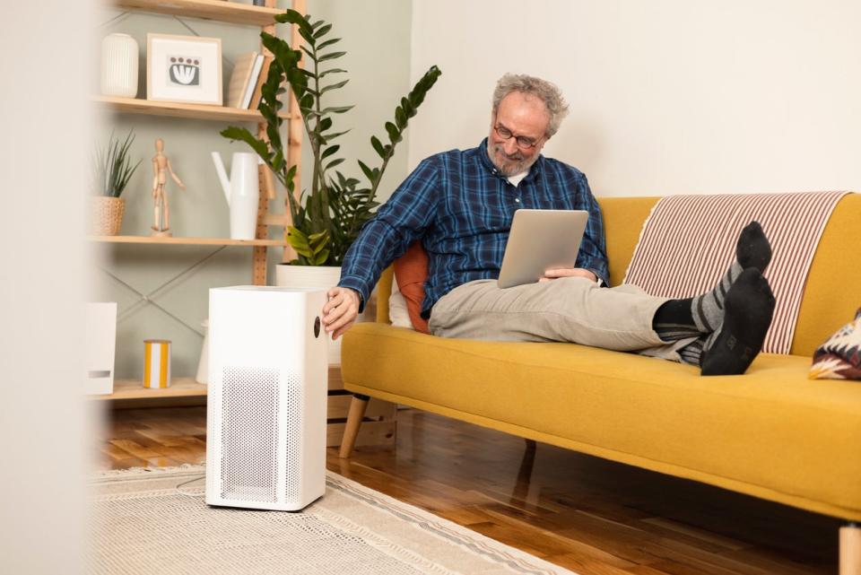 Man lounging on couch turning on an air purifier using a digital tablet