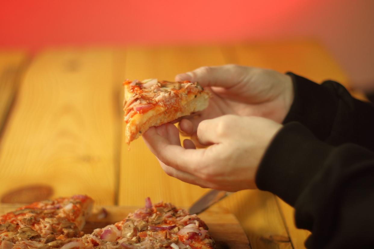 piece of pizza in the hands of a person over a table and a pink background