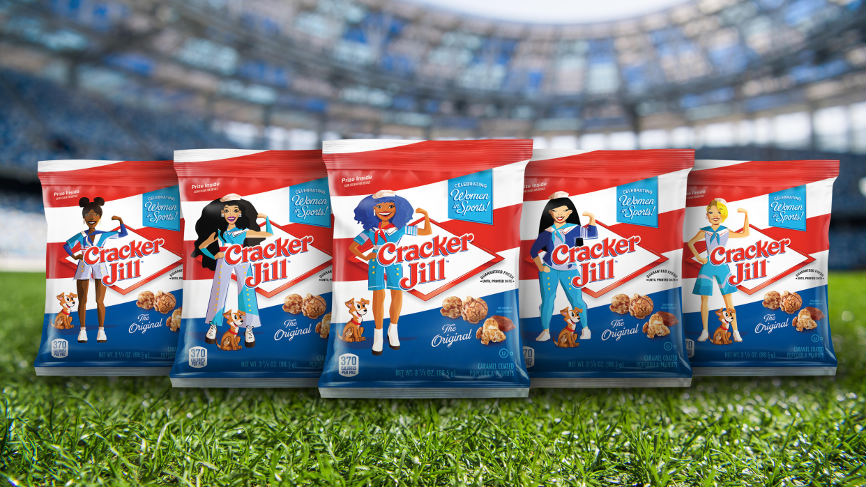 Five bags of Cracker Jills, each with a different cartoon girl on the front, showcasing diversity, on Astro Turf, stands of a stadium blurred in the background