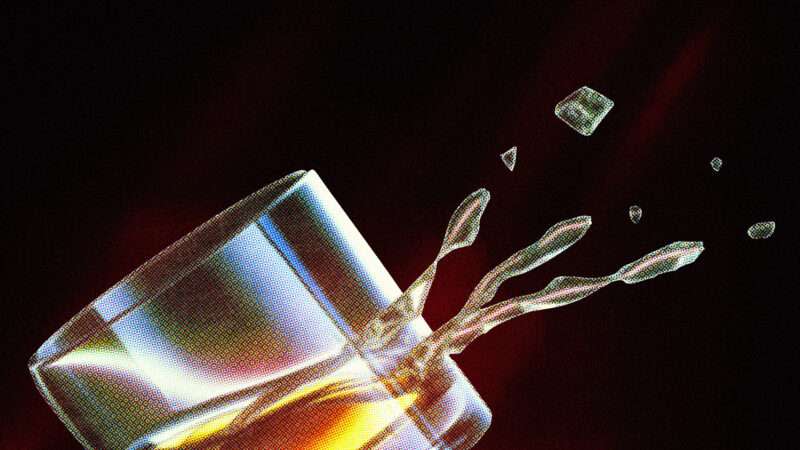 A glass of brown liquor tilted on a black background.