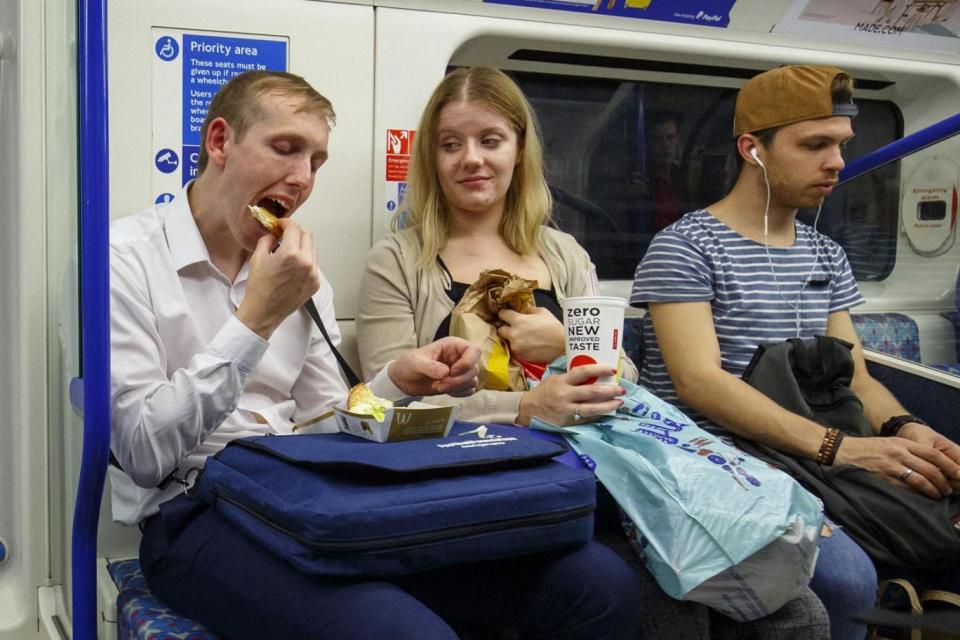 A commuter tucks into a McDonald's on the Tube while a friend looks on
