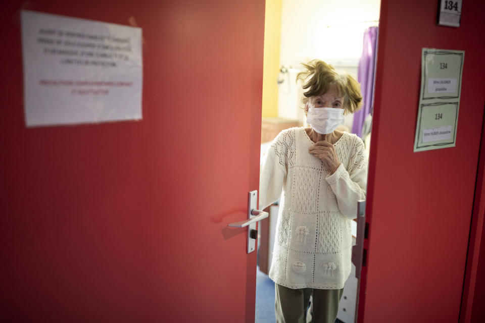 Jacqueline Huber wears a face mask as she looks out from a doorway at a care home in Kaysesberg, France Thursday April 16, 2020. The elderly make up a disproportional share of coronavirus victims globally, and that is especially true in nursing homes, which have seen a horrific number of deaths around the world. (AP Photo/Jean-Francois Badias)