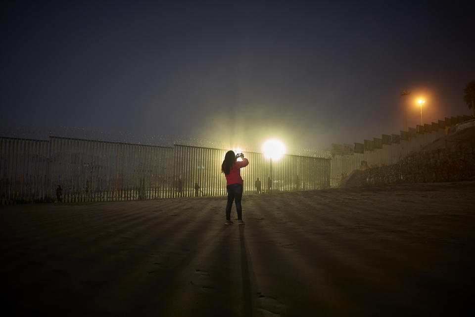 FILE - In this Jan. 10, 2019, file photo, a woman records with her phone, as floodlights from the United States light up the border wall, topped with razor wire along the beach in Tijuana, Mexico. The government is working on replacing and adding fencing in various locations, and Trump in February declared a national emergency to get more funding for the wall. (AP Photo/Gregory Bull, File)