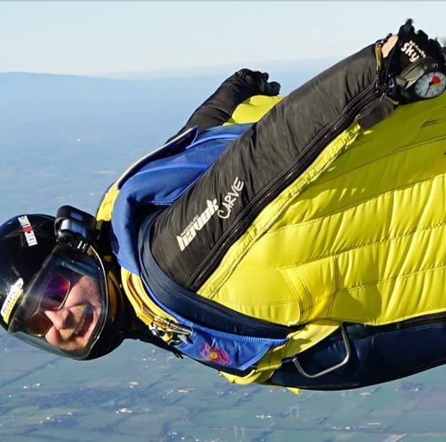 A close up photos of Arron Toepfer skydiving showing him looking at the camera smiling.