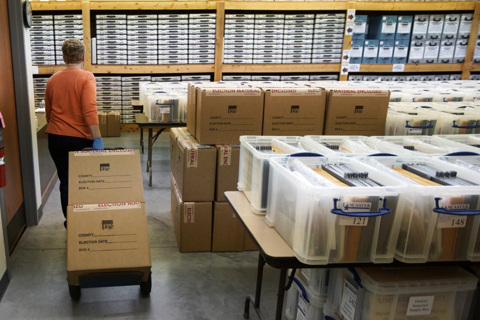 In this April 14, 2020 photo, Nadette Cheney wheels in boxes of printed ballots into the storage room of the Lancaster County Election Committee offices in Lincoln, Neb., where voting tables, ballot boxes and supplies are stored. Officials in Nebraska are forging ahead with plans for the state’s May 12 primary despite calls from Democrats to only offer voting by mail and concerns from public health officials that in-person voting will help the coronavirus spread. Republican leaders have encouraged people to request absentee ballots but say polling places will be open. (AP Photo/Nati Harnik)