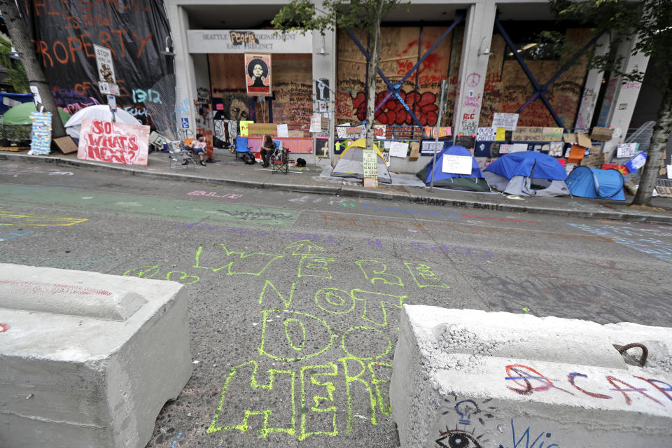 Street graffiti reads "We're Not Done Here," Wednesday, June 24, 2020, in front of the Seattle Police East Precinct building inside the CHOP (Capitol Hill Occupied Protest) zone in Seattle. The area has been occupied since a police station was largely abandoned after clashes with protesters, but Seattle Mayor Jenny Durkan said Monday that the city would move to wind down the protest zone following several nearby shootings and other incidents that have distracted from changes sought by peaceful protesters opposing racial inequity and police brutality. (AP Photo/Ted S. Warren)