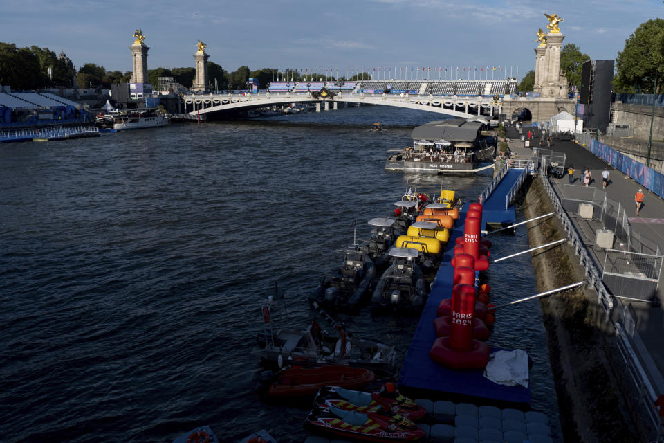 Watercraft and buoys sit along the Seine river as the triathlon event venue on the Pont Alexandre III bridge stands in the background at the 2024 Summer Olympics, Sunday, July 28, 2024, in Paris. (AP Photo/David Goldman)