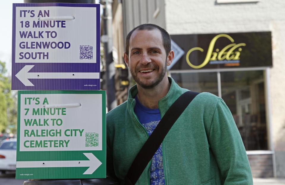 CORRECTS SPELLING OF TOMASULO - Matt Tomasulo poses for a photo by some of his signs in downtown Raleigh, N.C., Wednesday, April 11, 2012. On a January night he and friends put up 27 signs that advised people how to walk to various locations. The project, part of his master's thesis, has taken off with city officials, with two other states now planning to use his signs. (AP Photo/Gerry Broome)