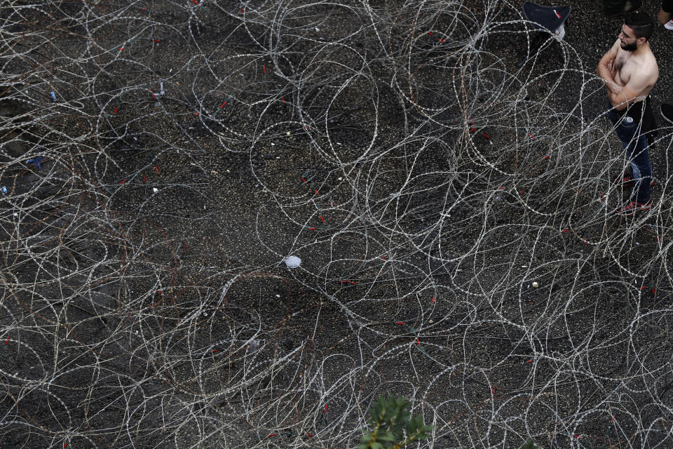 An anti-government protester stands next to a barbed-wire barrier that was set up to close a road leading to the government palace, in Beirut, Lebanon, Wednesday, Oct. 23, 2019. Lebanese troops have moved in to open several major roads in Beirut and other cities, scuffling in some places with anti-government protesters who had blocked the streets for the past week. (AP Photo/Hussein Malla)