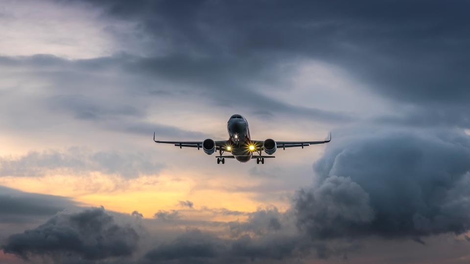 an airplane with lights on landing with a stormy background