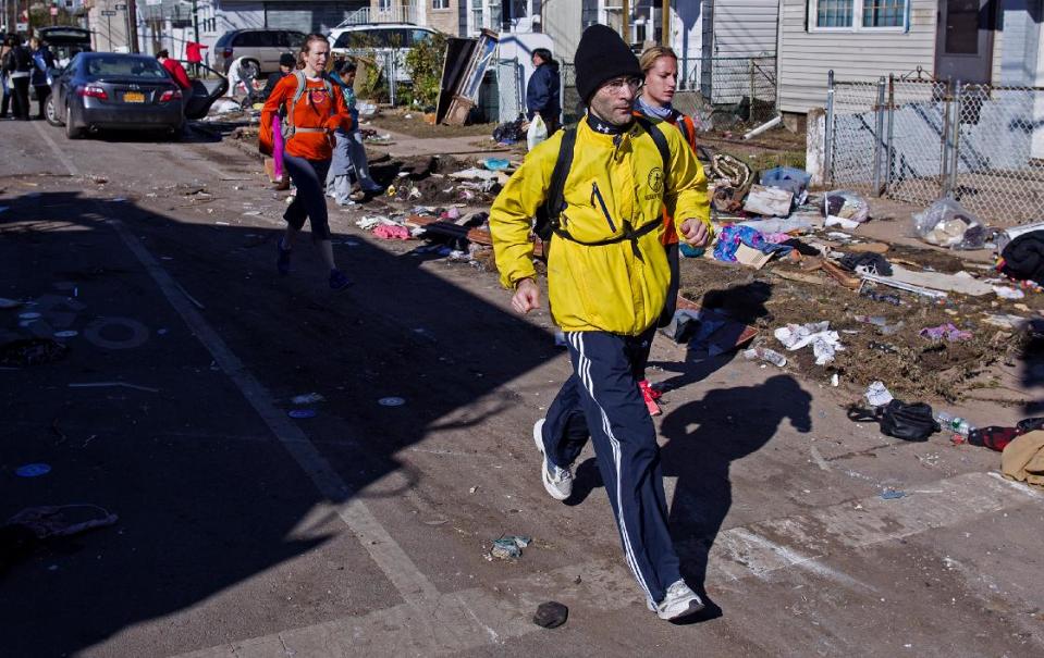 Carrying a backpack with goods and supplies, marathon runner Eitan Tabak runs past debris in the hard hit Midland Beach neighborhood of the Staten Island borough of New York, Sunday, Nov. 4, 2012. Background right is marathon runner Michelle Mascioli and far left marathon runner Rachel Wheeler of New York. With the cancellation of the New York Marathon, hundreds of  runners, wearing their marathon shirts and backpacks full of supplies, took the ferry to hard-hit Staten Island and ran to neighborhoods hard hit by Superstorm Sandy to help. (AP Photo/Craig Ruttle)