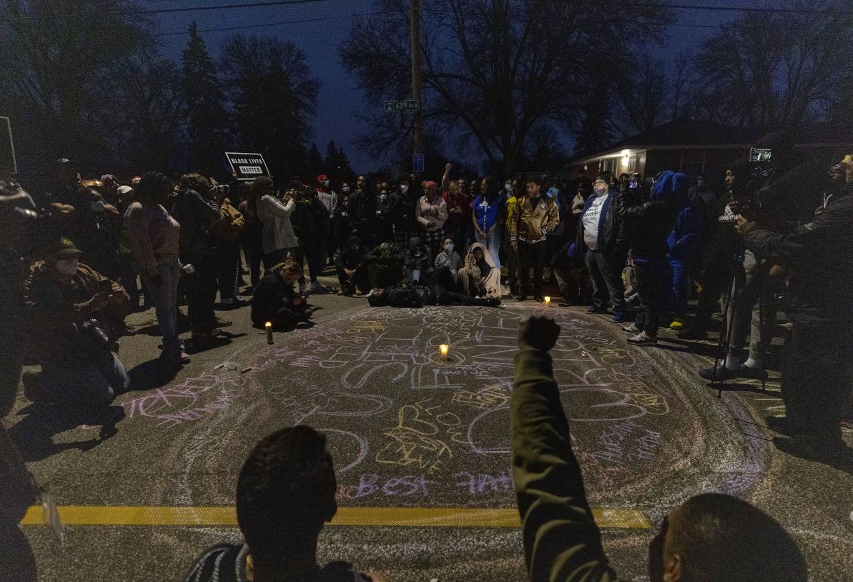 A crowd forms a circle around a memorial for Daunte Wright in Brooklyn Center, Minn., Sunday, April 11, 2021. Wright's family told a crowd that he was shot by police Sunday before getting back into his car and driving away, then crashing the vehicle several blocks away. The family said Wright was later pronounced dead.