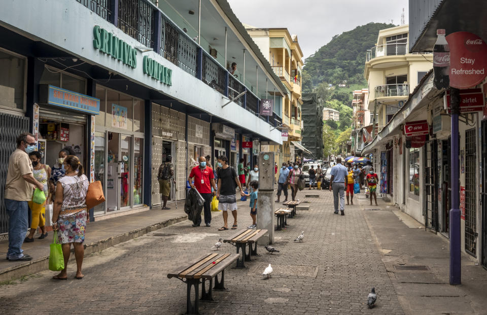 Pedestrians wear masks as they walk on a street in the capital Victoria, Mahe Island, Seychelles Thursday, Feb. 25, 2021. The president of the Indian Ocean island nation of Seychelles says he hopes enough residents will soon be vaccinated against COVID-19 to stop the spread of the virus, hoping to achieve herd immunity by mid-March by vaccinating about 70% of the population. (AP Photo/Salim Ally)