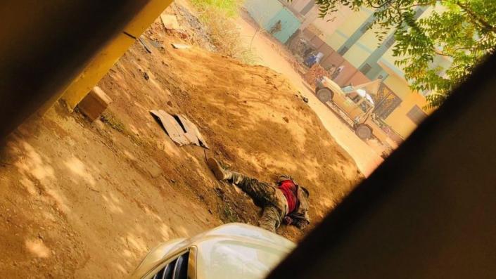 The body of a soldier lies next to a mound of dirt as a soldier uses a building for cover across the street in Khartoum on April 15, 2023, as fighting intensifies