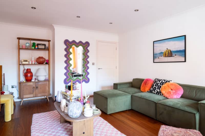 Green couch with colorful pillows anchors white living room.