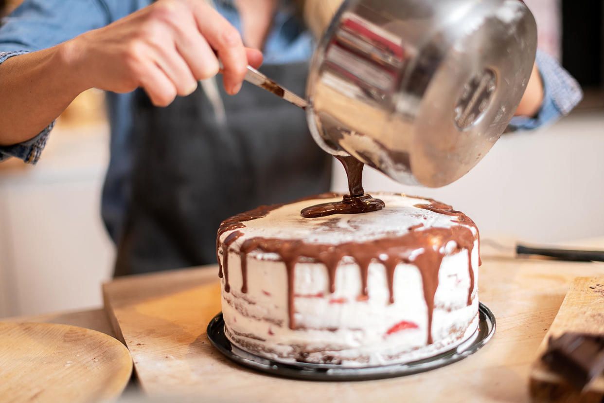 Woman decorating chocolate sponge cake (ilbusca / Getty Images)