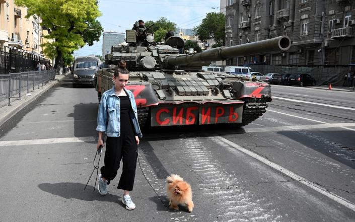 A woman with a dog walks past a tank as fighters of Wagner private mercenary group are deployed in a street near the headquarters of the Southern Military District in the city of Rostov-on-Don