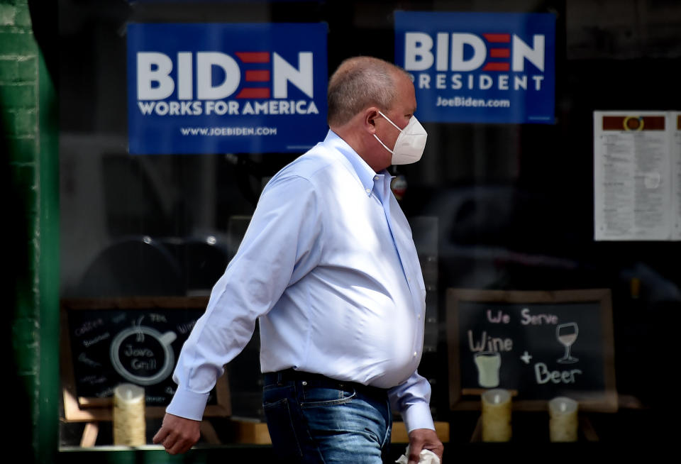 A man wearing a face mask walks past signs for Joe Biden's 2020 presidential campaign amid the coronavirus outbreak on May 11, 2020 in Alexandria, Virginia. (Photo by Olivier DOULIERY / AFP) (Photo by OLIVIER DOULIERY/AFP via Getty Images)