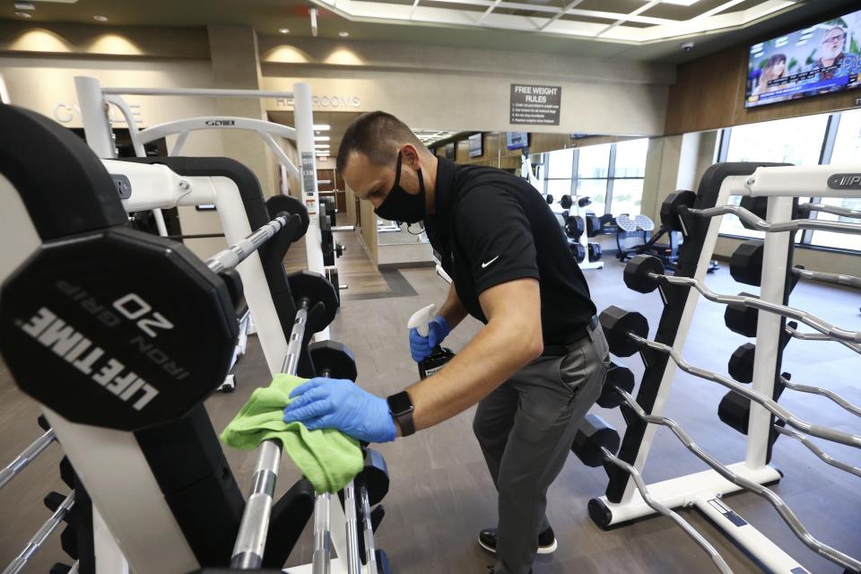 Jason Nichols, facilities operation manager, disinfects equipment at the Life Time Biltmore as it opens for business after being closed due to the coronavirus Monday, May 18, 2020, in Phoenix. Big-box gyms and local fitness studios are reopening under a patchwork of protocols based on state and local guidance, but most are following these basics: spacing out cardio machines, touchless entry, smaller class sizes, increased cleaning and requiring users to clean all equipment before and after each use. (AP Photo/Ross D. Franklin)