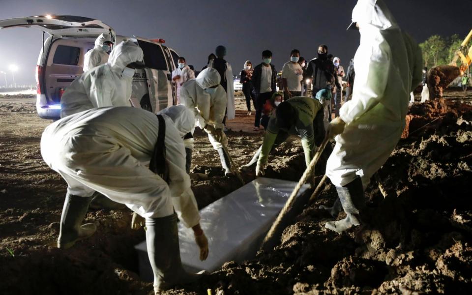 Gravediggers wearing personal protective equipment (PPE) burry a coffin as relatives stand behind at Muslim burial area provided by the government for coronavirus disease (COVID-19) victims, in Jakarta, Indonesia, July 7, 2021.  - Reuters