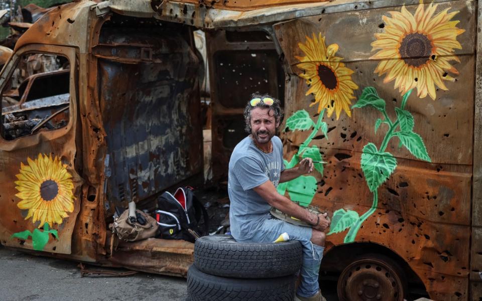 Los Angeles artist Trek Kelly paints a car destroyed a Russian attack - GLEB GARANICH/REUTERS