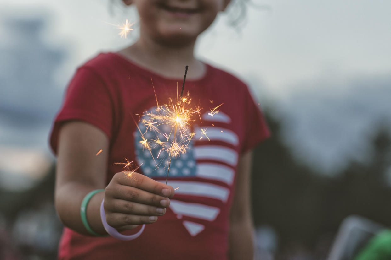 Child in a American-flag-themed T-shirt holds a burning sparkler.