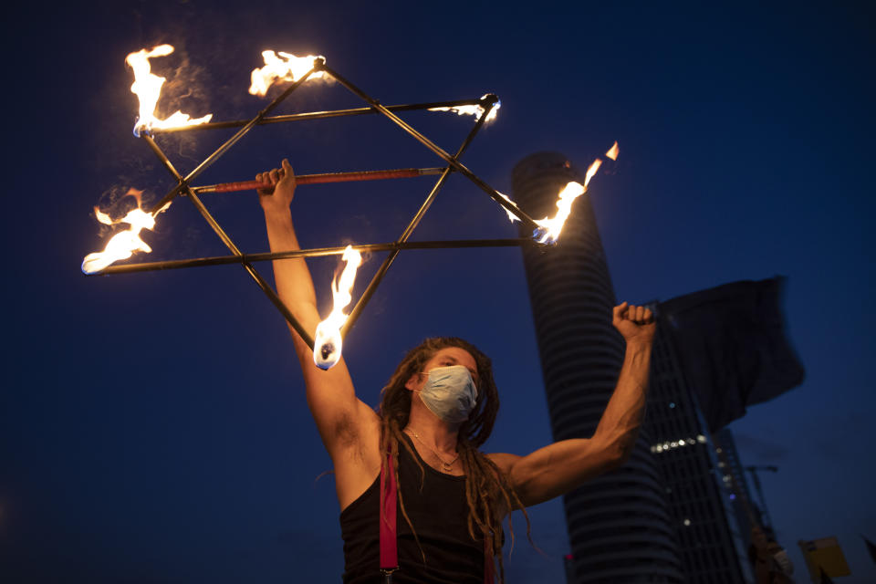An Israeli juggler holds model in a shape of Star of David on a bridge during a protest against Israel's Prime Minister Benjamin Netanyahu in Tel Aviv, Israel, Saturday, Aug. 22, 2020. (AP Photo/Oded Balilty)