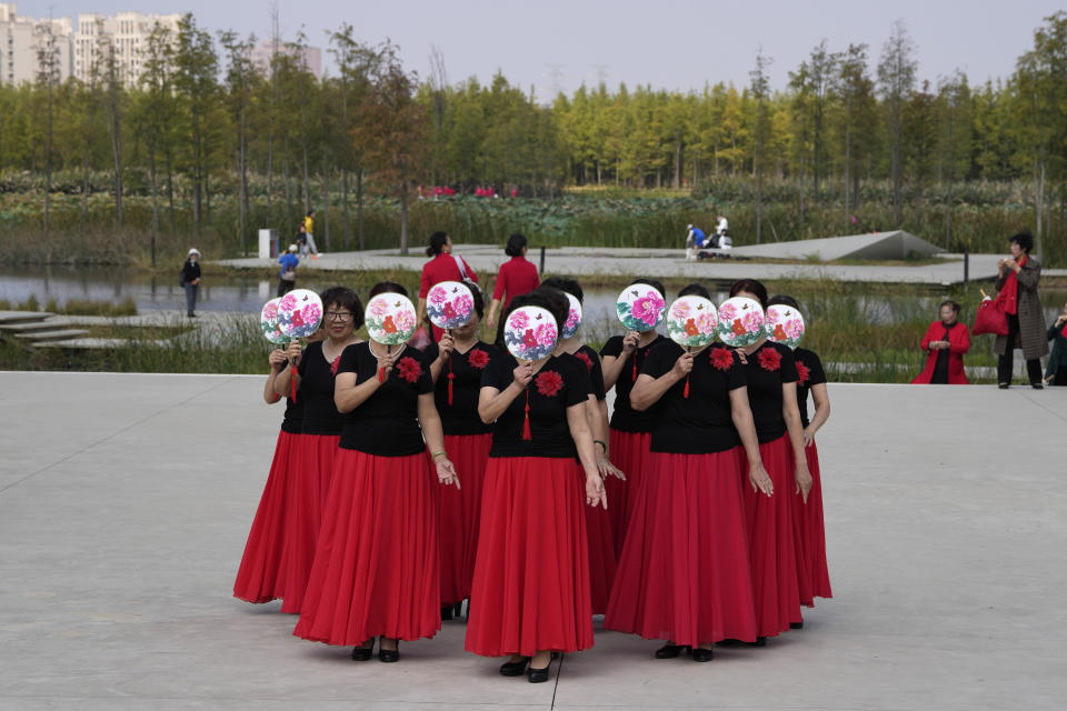 Residents hold up fans with flower designs to hide their faces as they dance at the "Fish Tail" sponge park that's built on a former coal ash dump site in Nanchang in north-central China's Jiangxi province on Sunday, Oct. 30, 2022. The concept of the park involves creating and expanding parks and ponds within urban areas to prevent flooding and absorb water for times of drought. (AP Photo/Ng Han Guan)