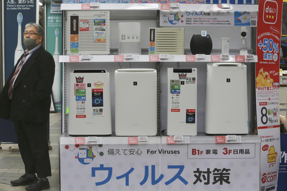 A man wearing a face mask to protest against the coronavirus stands beside a display of air cleaners at an electronics retailer in Tokyo, Tuesday, Jan. 12, 2021. The Tokyo area has been under a state of emergency since Friday to try to stop the spread of the virus. The banner at bottom reads: "Antivirus." (AP Photo/Koji Sasahara)