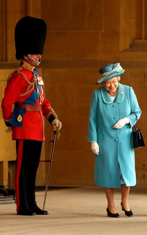 Queen Elizabeth II gets a fit of the giggles as she walks past her husband Prince Philip, standing to attention in his uniform and bearskin hat at Buckingham Palace in 2005 - Credit: Anwar Hussein/Getty Images