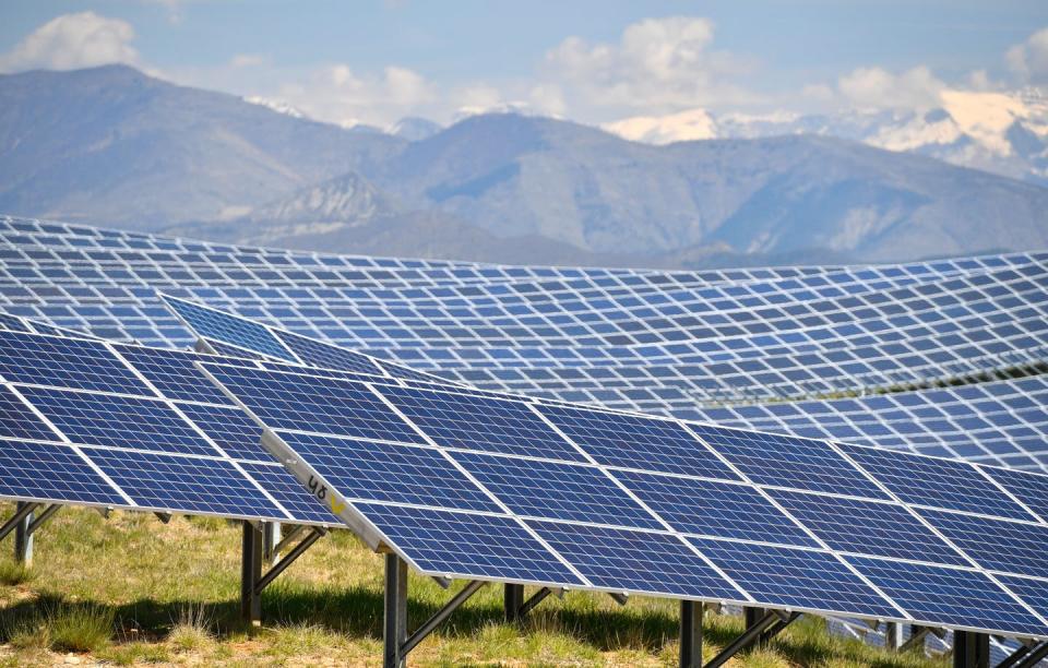 Rows of solar panels curve along a hillside with mountains in the background.