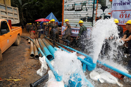 Soldiers and rescue workers walk past water pumped out of Tham Luang cave complex, where members of an under-16 soccer team and their coach have been found alive, in the northern province of Chiang Rai, Thailand, July 5, 2018. REUTERS/Soe Zeya Tun