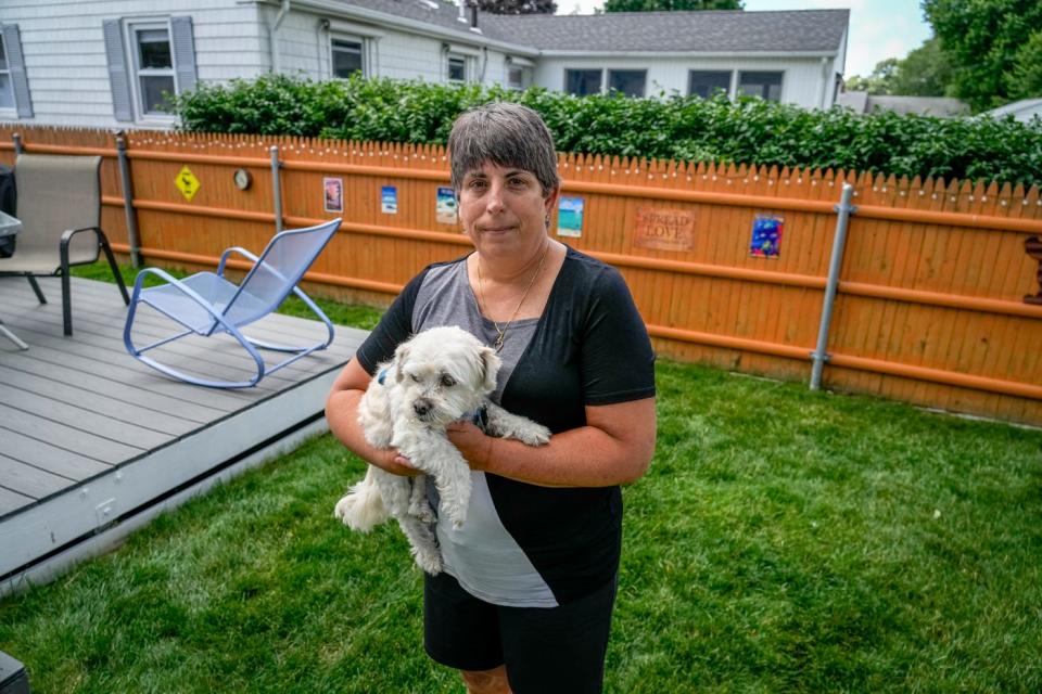 Linda Loxley, with dog Dante, in the backyard of her North Providence home. Lingering headaches and muscle, nerve and joint pain have left her debilitated and unable to work, more than a year after her bout with COVID-19.