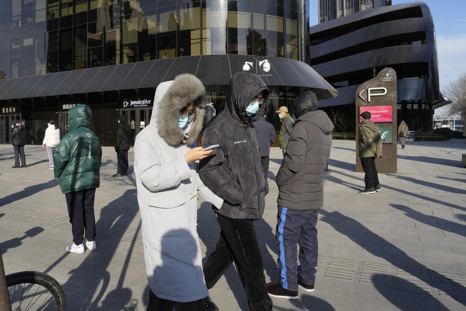 Residents wearing masks walk past others in line for COVID tests in Beijing, Wednesday, Dec. 7, 2022. In a sharp reversal, China has announced a series of measures rolling back some of the most draconian anti-COVID-19 restrictions. (AP Photo/Ng Han Guan)