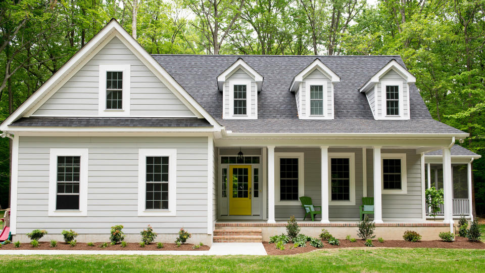 Exterior of a new Cape Cod styled suburban house with recently planted shrubs and grass.