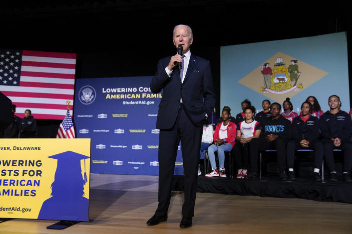 President Biden at the microphone with two rows of students sitting behind him and a large poster board saying: Lowering Costs for America Families.
