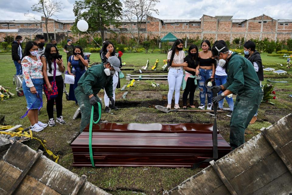 Two groups of young women stand together, looking over men securing the wooden coffins that they will lower into the ground.