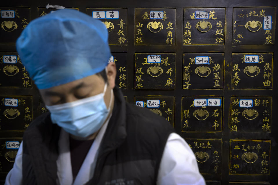 In this March 13, 2020 photo, a worker fills orders for prescriptions in front of a cabinet of drawers containing ingredients for traditional Chinese medicine preparations at the Bo Ai Tang traditional Chinese medicine clinic in Beijing. With no approved drugs for the new coronavirus, some people are turning to alternative medicines, often with governments promoting them. (AP Photo/Mark Schiefelbein)