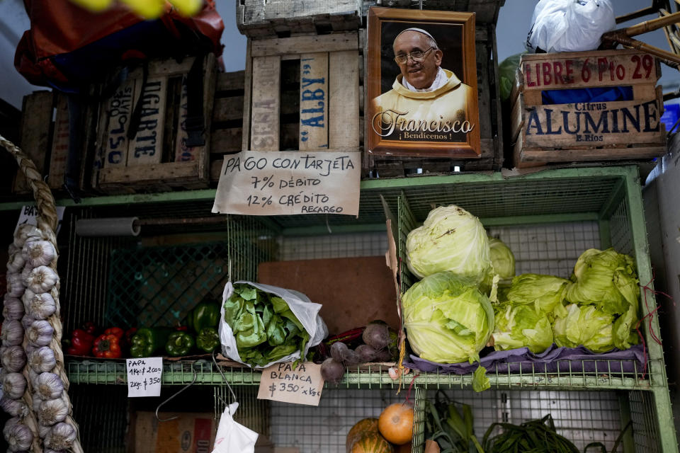 Una imagen del papa Francisco cuelga junto a un cartel que dice en español "Pago con tarjeta 7% débito, 12% crédito", en un mercado de frutas y verduras en Buenos Aires, Argentina, el jueves 11 de mayo de 2023. Según un reciente Informe de Seguridad Alimentaria del Banco Mundial, Argentina ha visto una tasa de inflación anual del 107% en los precios de los alimentos. (Foto AP/Natacha Pisarenko)