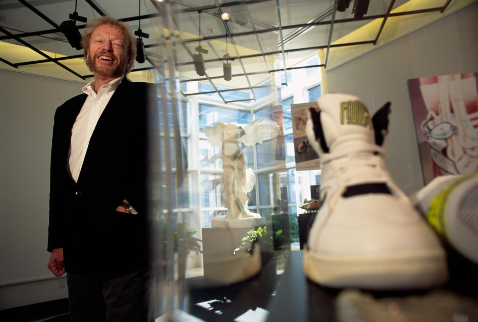 Nike President and CEO Phil Knight standing next to a pair of sneakers on display in a gallery.