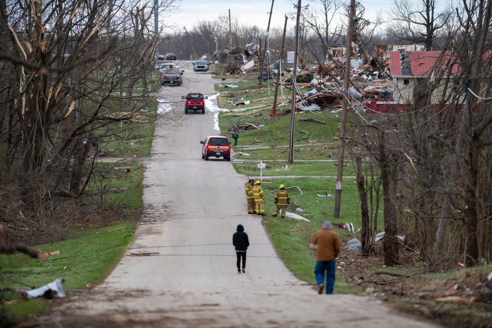 First responders and residents in Sullivan, Ind., walk and stand along a road where damage from a late-night tornado is seen on Saturday, April 1, 2023. (AP Photo/Doug McSchooler)