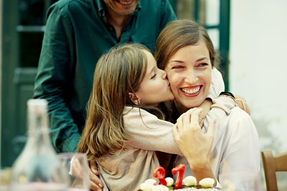 cute girl kissing mother on cheek while celebrating at outdoor table in yard