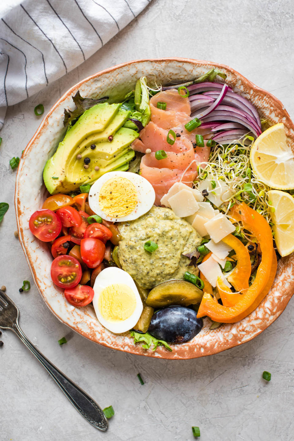 A hummus bowl with lots of vegetables, hard boiled egg, smoked salmon, and cheese.