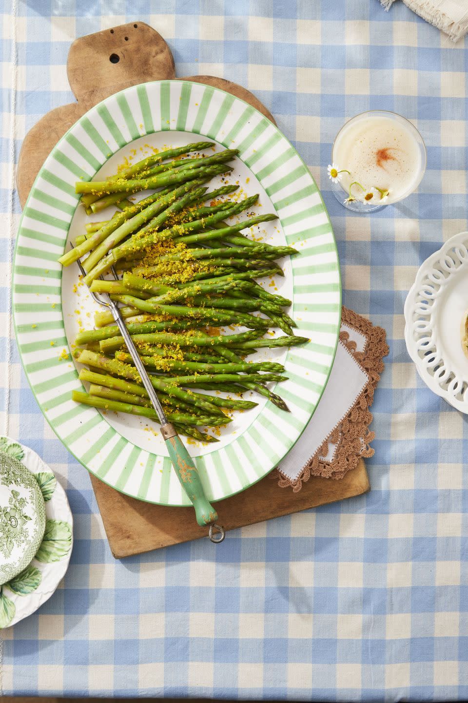 salt cured egg yolks over steamed asparagus on an oval pattern with a serving utensil