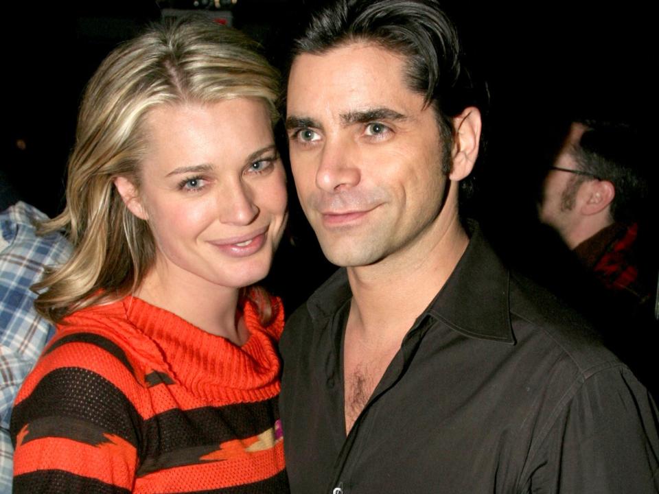 Rebecca Romijn, in a multicolored sweater and jeans, poses for photos with John Stamos, in a black shirt.