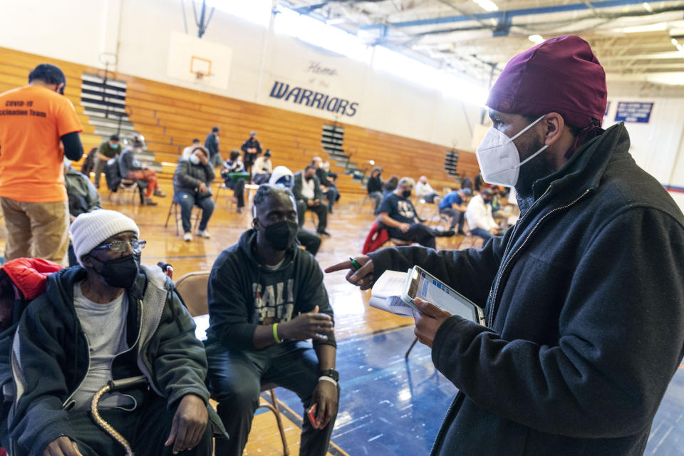 Dr. Eugenio Fernandez, right, checks on his patients, Baffour Ankoman Jr., 45, right, and his father, Baffour Ankoman Sr., 77, after they were vaccinated at a clinic in Central Falls, R.I., Saturday Feb. 6, 2021. The city's main vaccination site, held every Saturday at the high school gymnasium, is an almost entirely volunteer operation. Even the roughly 800 shots administered weekly are donated by Fernandez. (AP Photo/David Goldman)